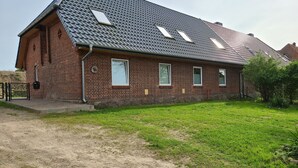 Ein Gebäude aus Backsteinen mit einem geneigten Dach, mehreren Fenstern und einem kleinen Garten.