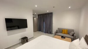 Et moderne hotelværelse med en stor seng, et fladskærms-tv på væggen, en sofa med puder og et lille bord.