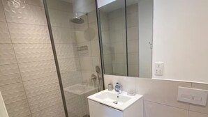 Et moderne badeværelse med en glasafskærmet brusekabine, en hvid vask og et toilet.