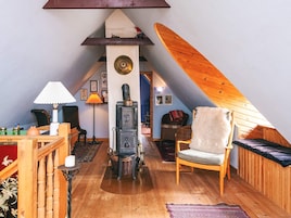 Acogedor cuarto en el ático con piso de madera, chimenea, una silla y una cama.