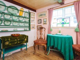 Una habitación con piso de madera, una mesa verde con mantel verde, una silla de madera, un aparador antiguo color esmeralda y un escurridor de platos fijado a la pared.