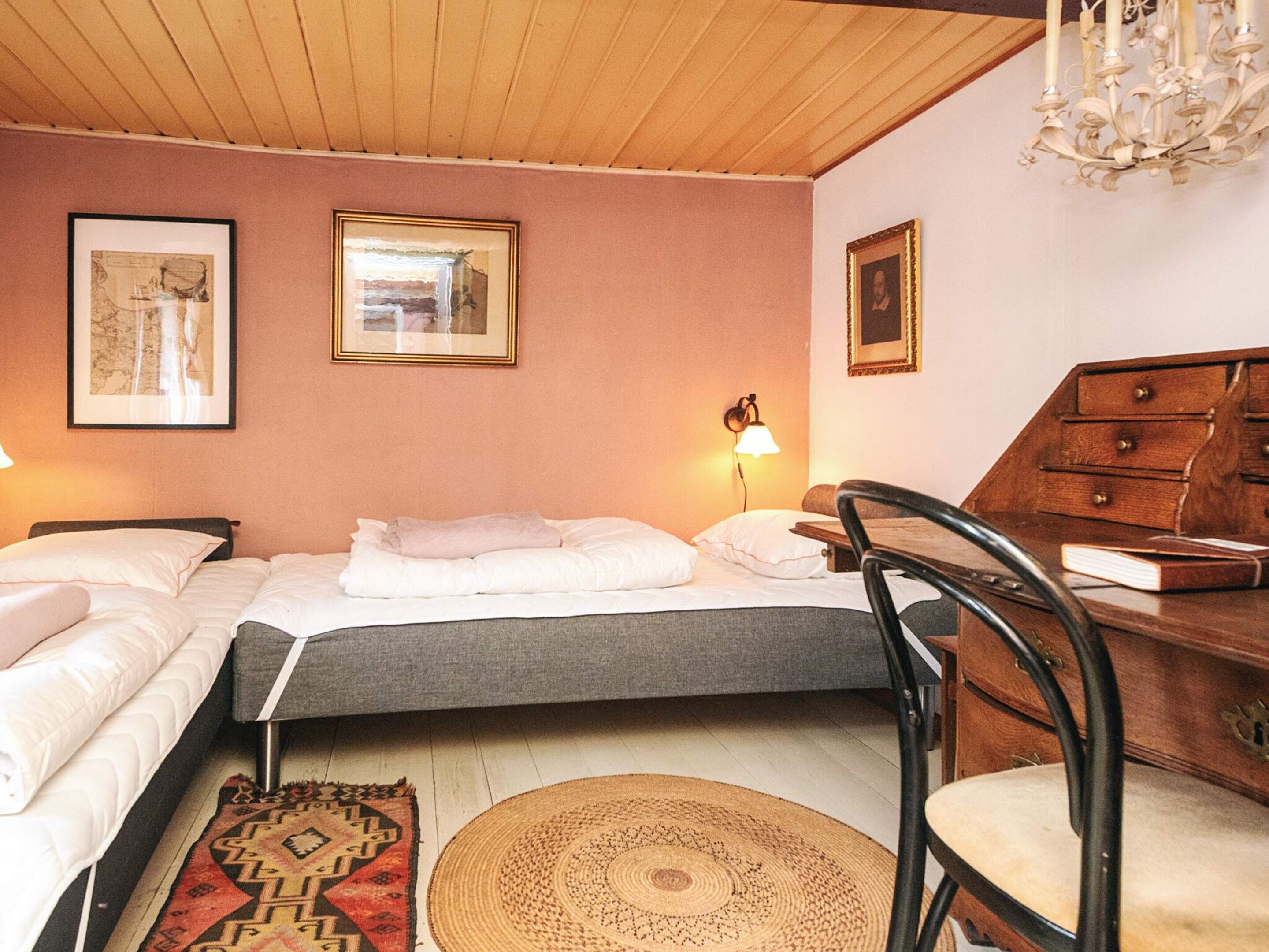 A hotel room with a bed, a desk with drawers, a chair, a lamp, and two framed pictures on the wall.