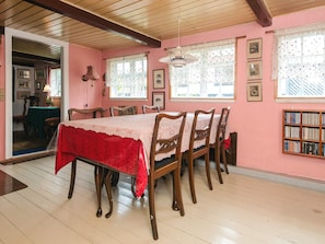 A dining room with a table set for six, wooden chairs, a red tablecloth, lace curtains, and a bookshelf against the wall. - 6 Person Holiday Home in Glesborg (Glesborg)