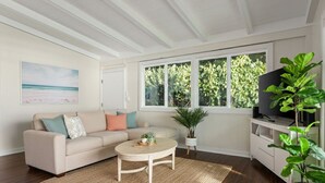 A living room with a beige sofa, a round coffee table, and a television on a white cabinet. - "Waimea Vista" | Oceanfront, Walkable to Beaches (Haleiwa)