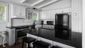 A modern kitchen with white cabinetry, a black refrigerator, a stove, and a microwave. - "Waimea Vista" | Oceanfront, Walkable to Beaches (Haleiwa)