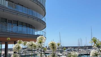 A modern building with a curved facade, a marina with boats, and lush greenery in the foreground.