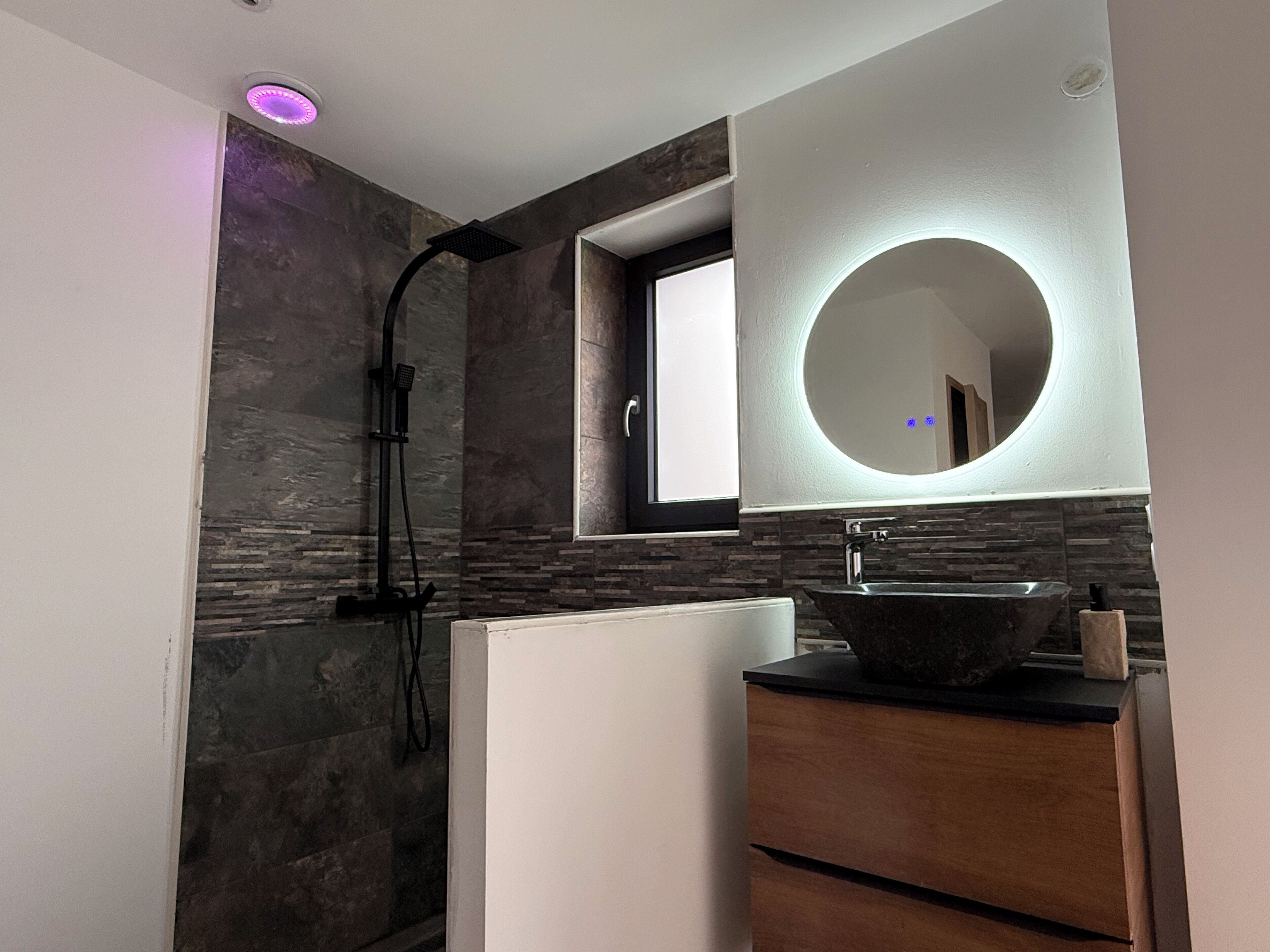 A modern bathroom with a stone wall, a built-in sink, and a shower with a black hose.