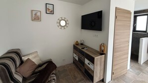 A small, modern living room with a sofa, a TV, a wooden cabinet, and a door leading to another room. - Chez Maud et Fab (Dinozé)