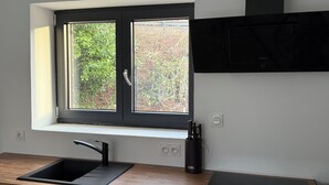 A modern kitchen with a black countertop, a sink, a window with a view of greenery, and a built-in stove. - Chez Maud et Fab (Dinozé)