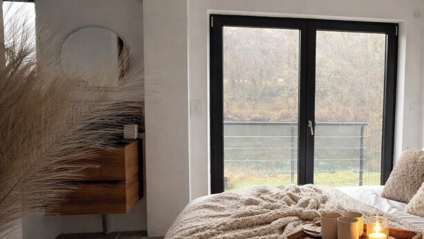 A bedroom with a large window, a bedside table with a tray of candles and mugs, and a cozy knitted blanket. - Chez Maud et Fab (Dinozé)