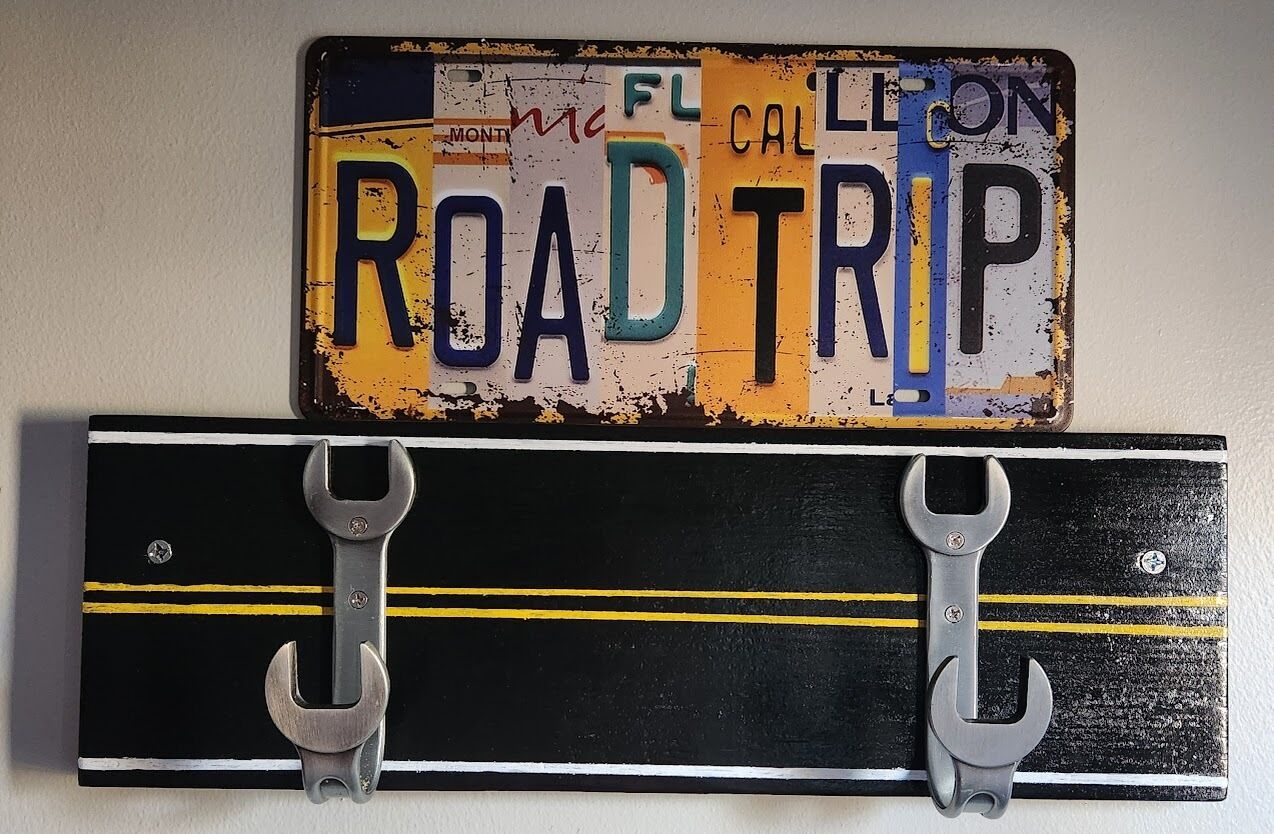 A license plate with the text "ROAD TRIP" and a black metal object with yellow lines and two metal hooks.