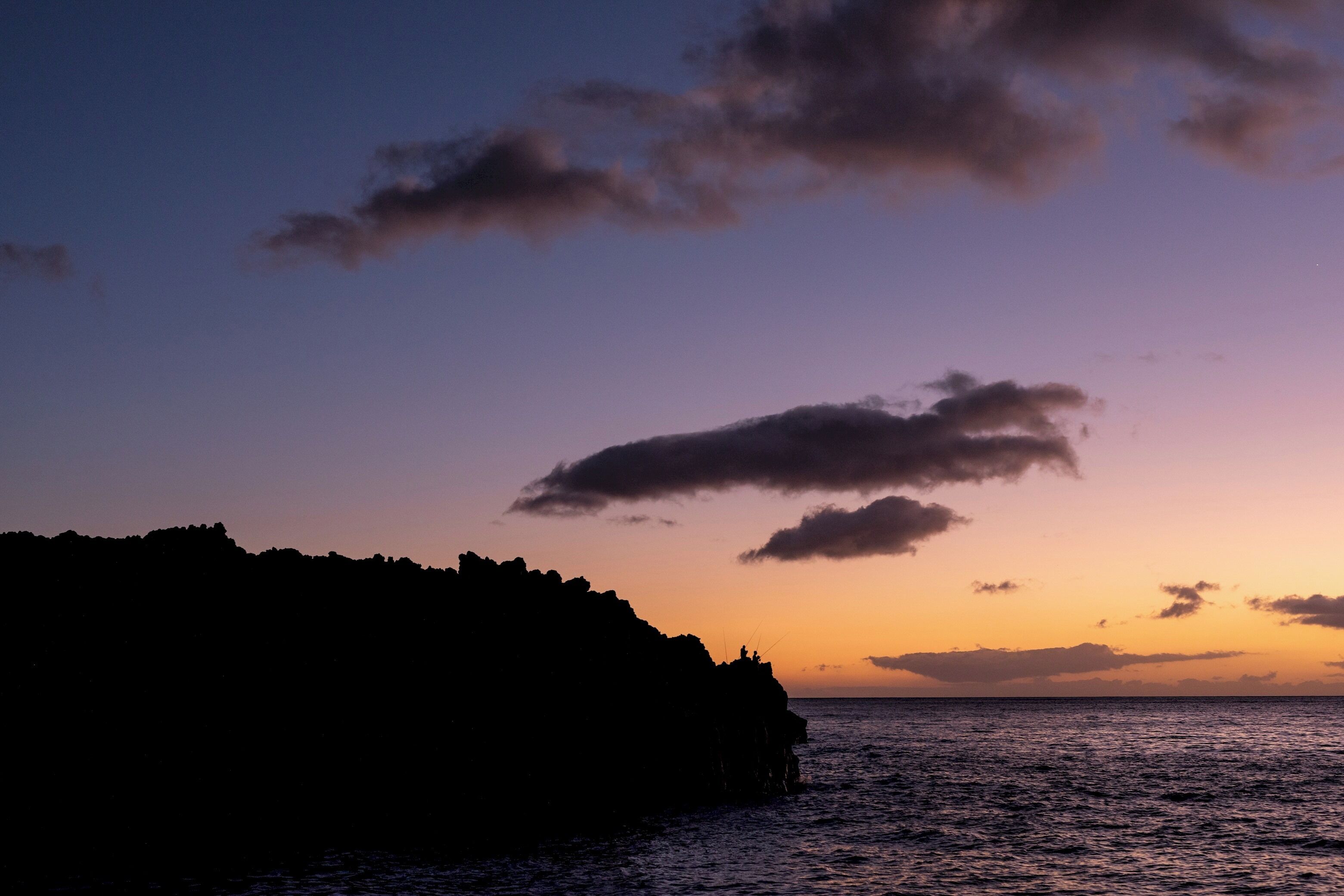 A coastal sunset with silhouettes of rocky cliffs and calm sea.
