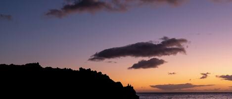A coastal sunset with silhouettes of rocky cliffs and calm sea.