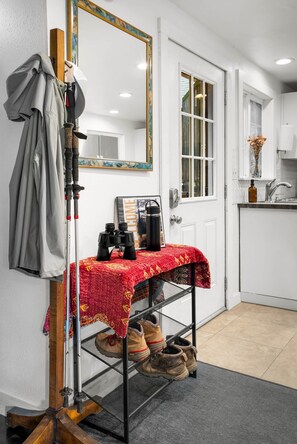 A room with a door, a coat rack, a table with binoculars, a pair of boots, and a mirror. - Family-Friendly Cabin Retreat w/ Private Hot Tub (Mason County)