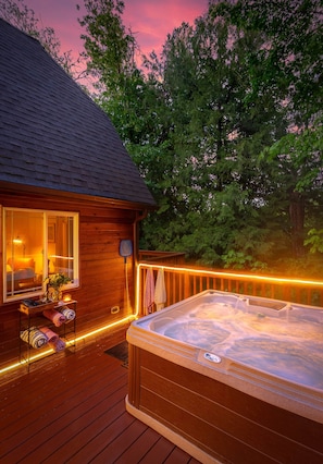 Eine Holzhütte mit Whirlpool, Terrasse und einem Fenster mit Blick auf einen Wald.