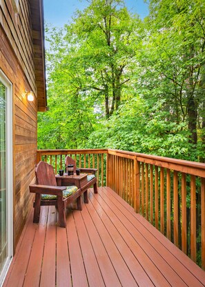 A wooden deck with a table and chairs, surrounded by a railing, overlooking a dense forest. - Family-Friendly Cabin Retreat w/ Private Hot Tub (Mason County)
