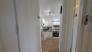 A narrow hallway leading to a kitchen with white cabinets, a microwave, and an oven. - digby house flat 1 (West Mersea)