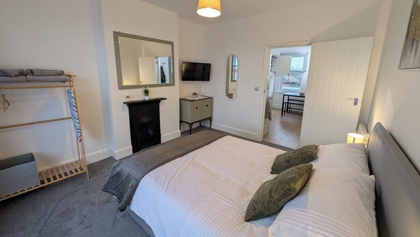 A bedroom with a bed, a dresser, a mirror, a television, and a door leading to a bathroom. - digby house flat 1 (West Mersea)