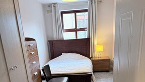 A bedroom with a bed, a chair, a dresser, a nightstand, and a window with curtains. - Spacious Apartment on a quiet street 1 min from Smithfield Square. (Dublin 7)