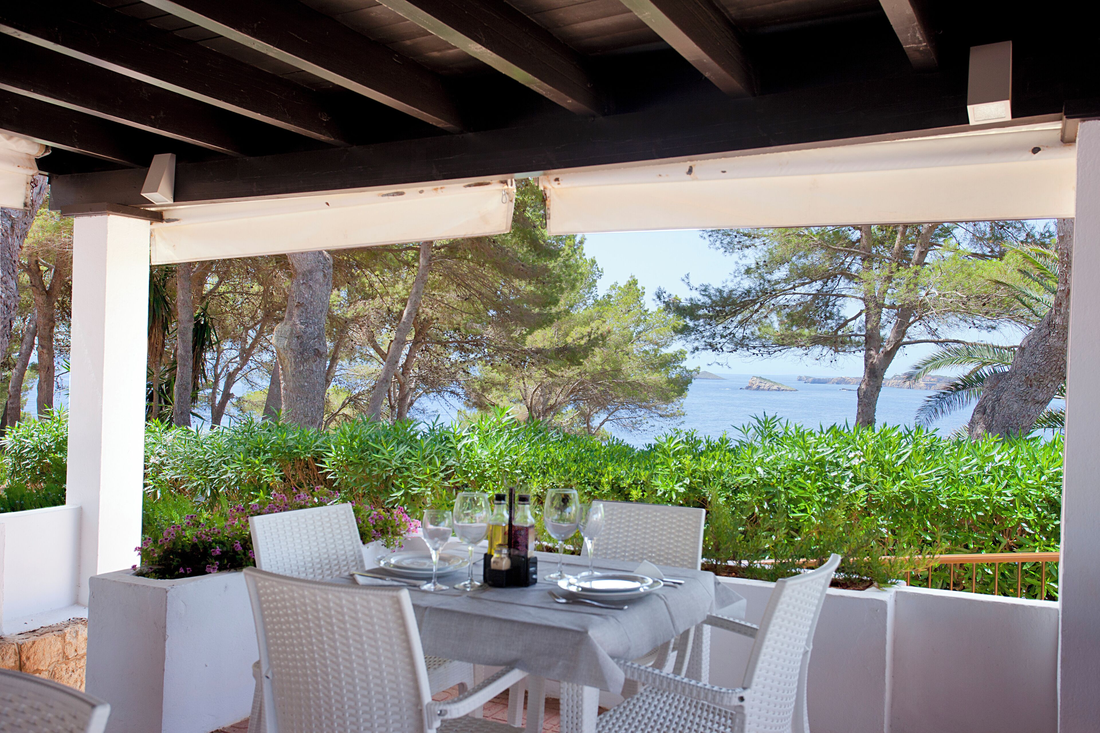 An outdoor dining area with a table set for four, overlooking a scenic view of the sea and trees.