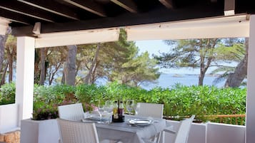 An outdoor dining area with a table set for four, overlooking a scenic view of the sea and trees.
