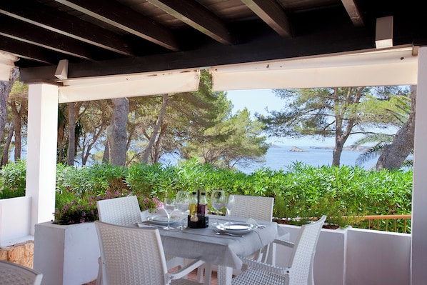An outdoor dining area with a table set for four, overlooking a scenic view of the sea and trees. - APARTAMENTOS CLUB CALA AZUL (Santa Eulalia del Rio)