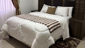Una cama bien hecha con un edredón estampado, un cabecero y una mesita de noche con una lámpara.