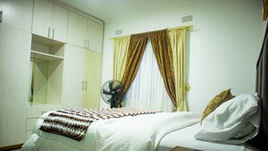Un dormitorio con cama, mesita de noche, armario y ventana con cortinas.