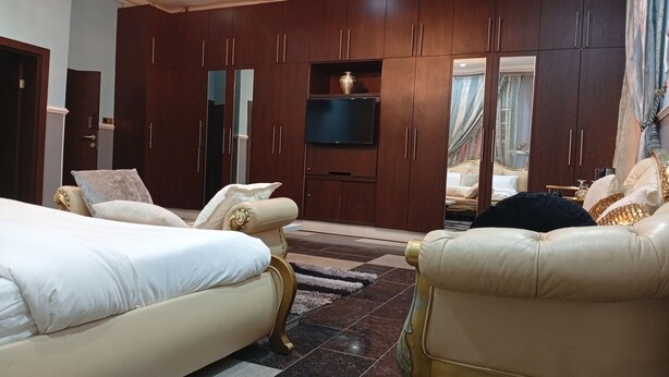 Een ruime slaapkamer met een groot bed, een bank en een aan de muur bevestigde televisie.