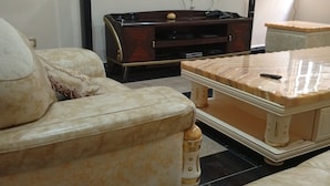 Een woonkamer met een beige bank, een salontafel en een aan de muur bevestigde televisie.