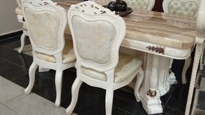 Een eetgedeelte met een marmeren tafel en sierlijke stoelen, een trap op de achtergrond en een betegelde vloer.