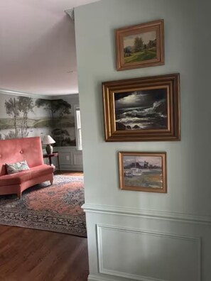 A living room with a pink sofa, a patterned rug, and three framed paintings on the wall. - Charming Home w/ Golf Cart Near Charleston & Beach--Monthly Stays (Mount Pleasant)