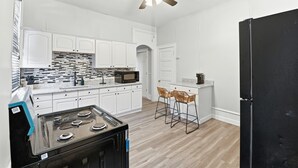 Une cuisine moderne avec des armoires blanches, une cuisinière noire, un ventilateur de plafond et un réfrigérateur noir.