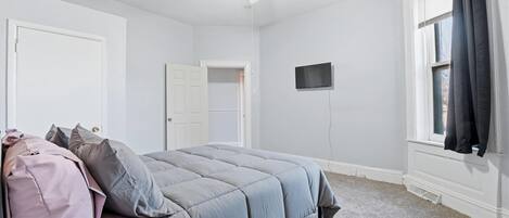 Un dormitorio con cama, ventilador de techo, televisor y ventana con cortinas.
