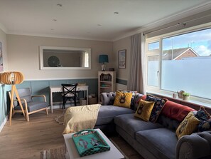 A cozy living room with a grey sofa, a wooden coffee table, and a desk with a chair. - Enjoyable 3-bedroom bungalow in charming Dymchurch perfect for relaxing (Dymchurch)