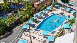 A large outdoor swimming pool with multiple lanes, surrounded by lounge chairs and umbrellas, and adjacent to a smaller pool and palm trees. - @ Marbella Lane Scenic Ocean & Lagoonview Studio (Honolulu)
