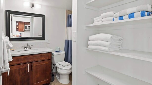 Ein Badezimmer mit Waschbecken, Spiegel, Toilette und Regalen mit gefalteten Handtüchern.