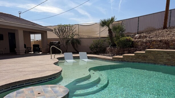A swimming pool with clear water, a tiled deck, and a stone wall.