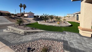 A residential area with a paved driveway, landscaped garden beds, and a lawn.