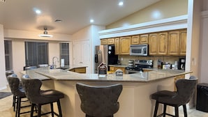 A modern kitchen with a central island, bar stools, stainless steel appliances, and wooden cabinets.