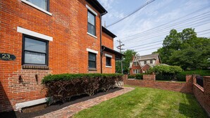A brick house with a number 23 sign, a small front yard with a hedge, and a neighboring house with a chimney. - German Village Studio: Charming & Pet-Friendly (Columbus)