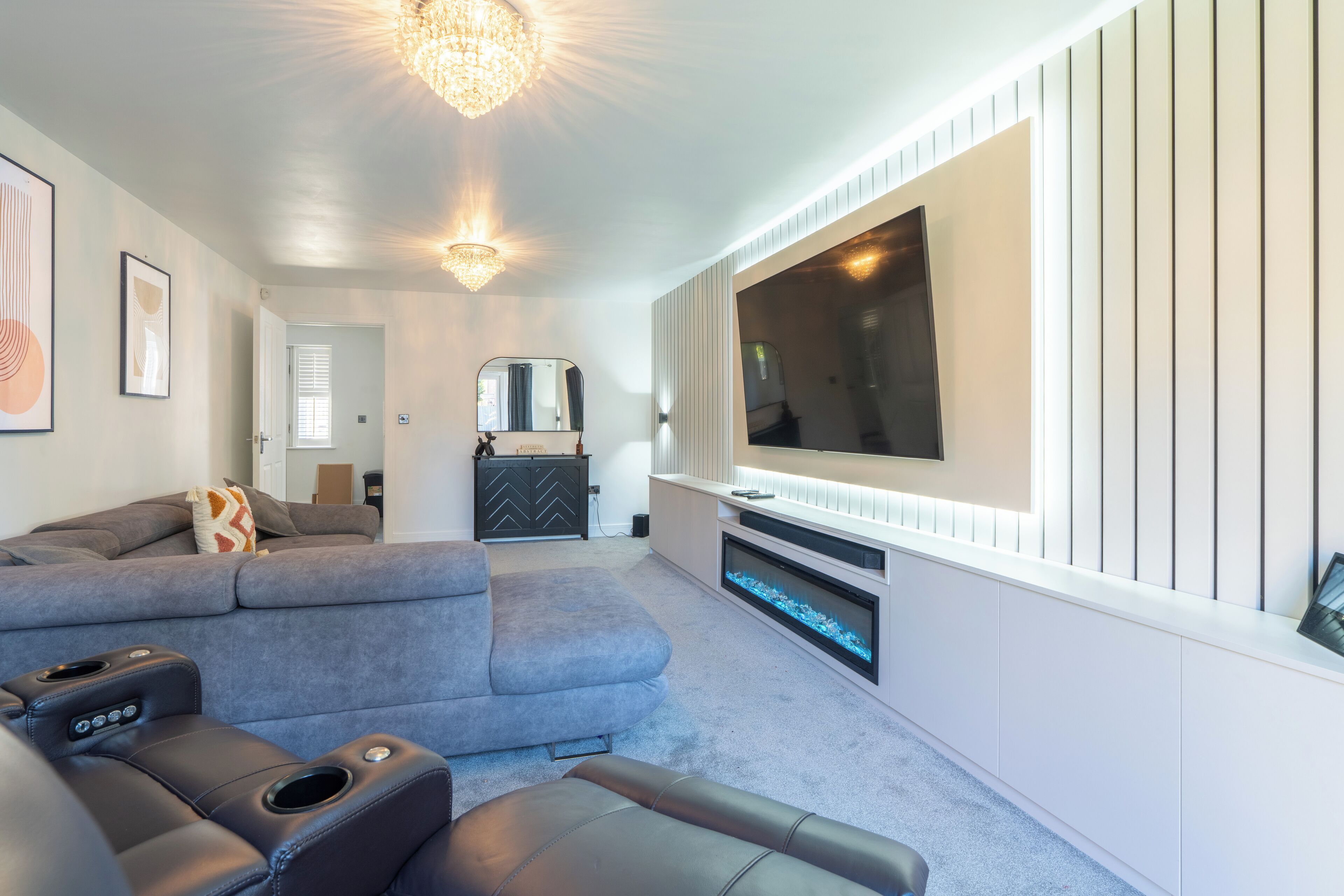 A modern living room with a sectional sofa, a flat-screen TV mounted on the wall, a fireplace, and a ceiling light fixture.