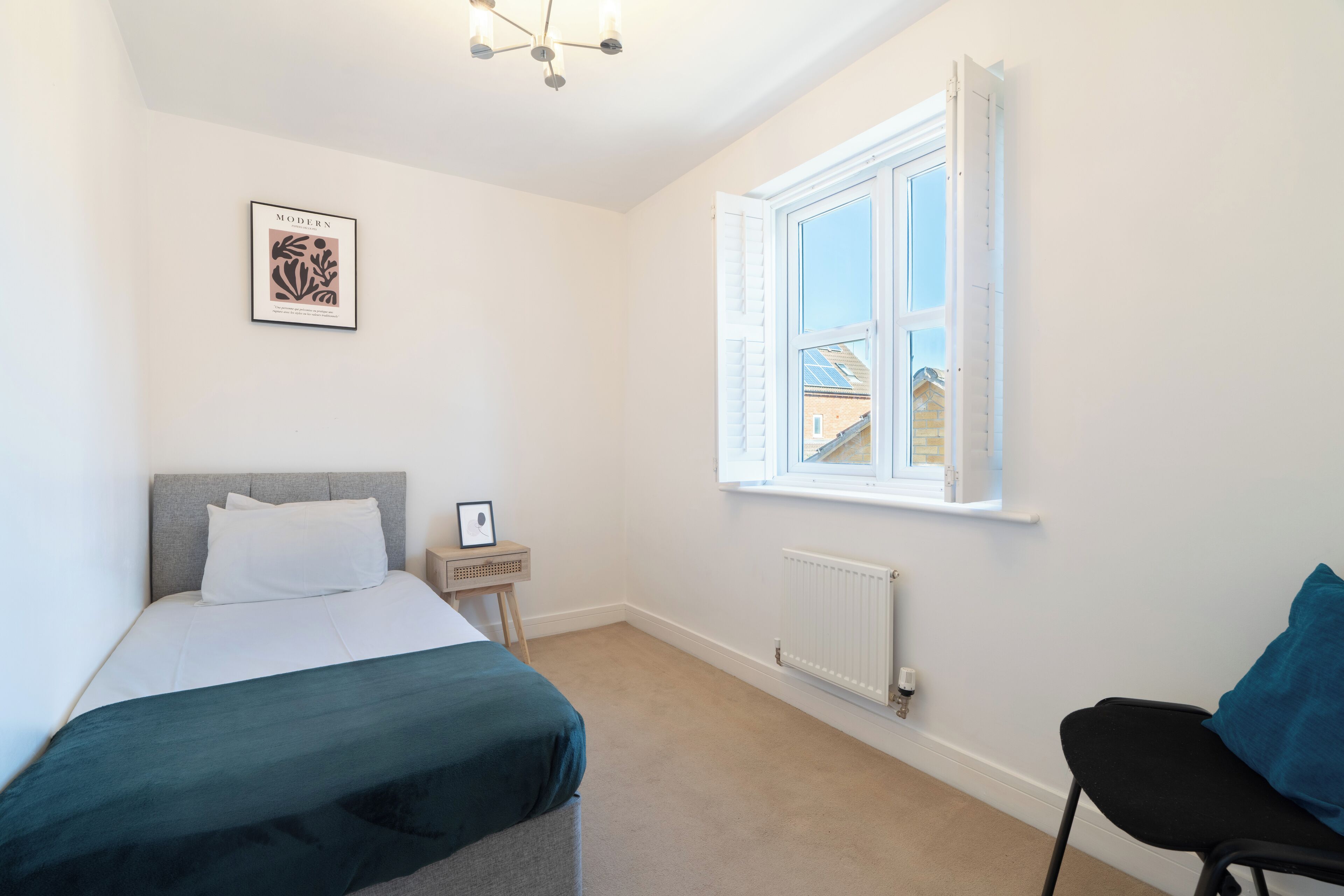 A bedroom with a bed, a nightstand, a chair, a window, and a radiator.