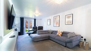 Un salon moderne avec un canapé d’angle gris, une table basse en verre et un téléviseur à écran plat fixé au mur.