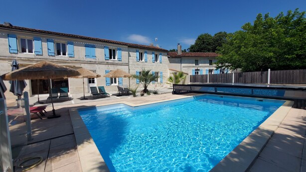 A swimming pool with lounge chairs and umbrellas, surrounded by stone buildings with blue shutters. - Typical house with pool and garden, quiet parking - Saintes Les Cuves (Chaniers)
