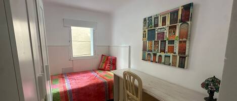 A bedroom with a bed, a desk, a chair, a window, and a ceiling light.
