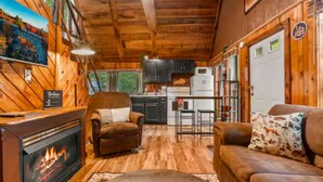 Ein gemütliches Blockhaus-Interieur mit Kamin, Holzwänden, einer Couch und einer Küchenzeile.