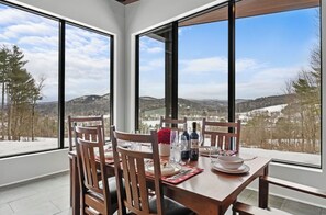 A dining area with a table set for four, large windows offering a view of a snowy landscape and hills.
