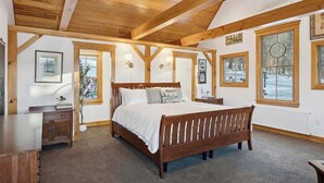 A bedroom with a wooden bed, a nightstand, a dresser, and a window with a view of trees.