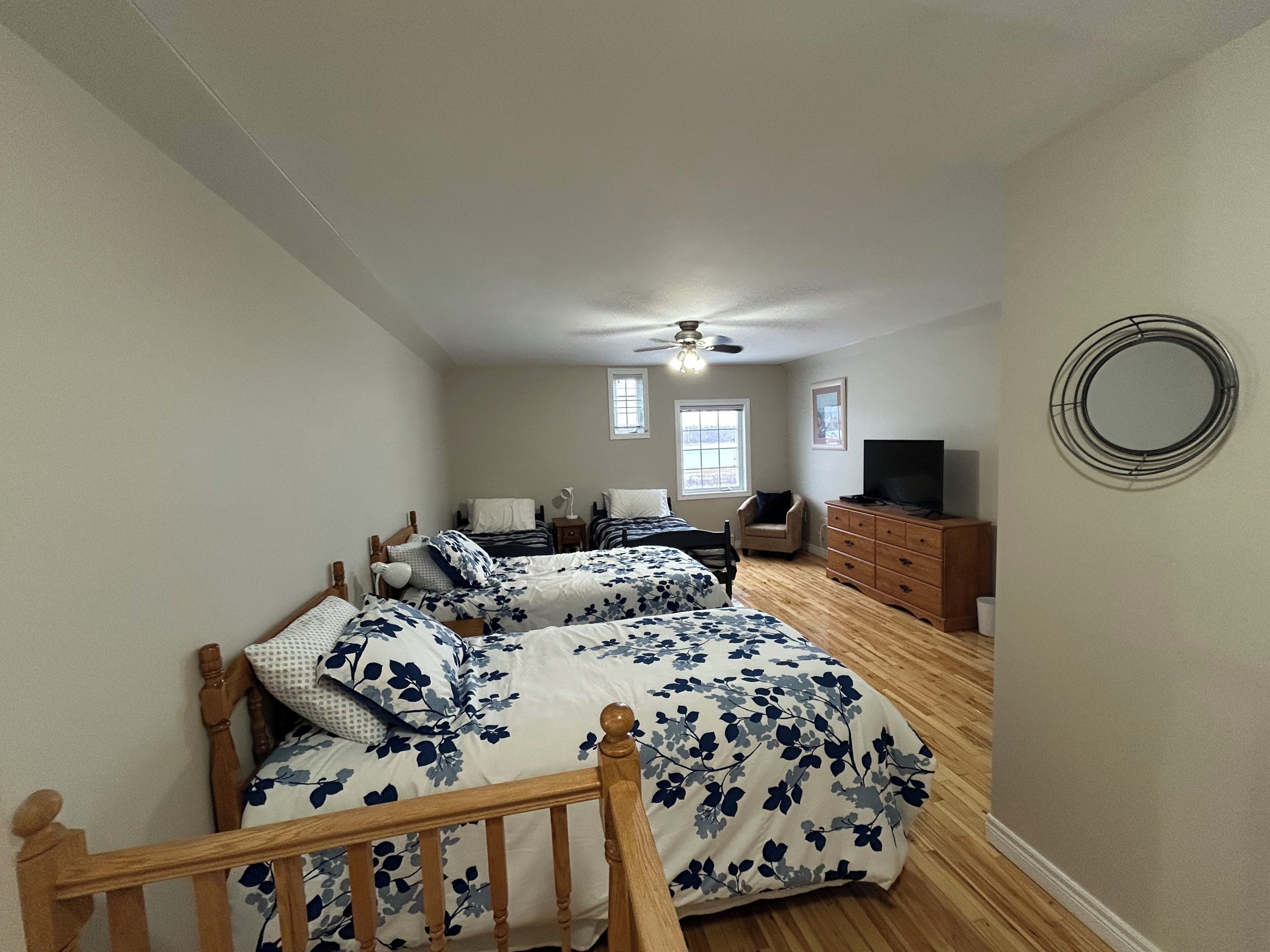 A bedroom with two beds, a chair, a dresser, a TV, and a ceiling fan.